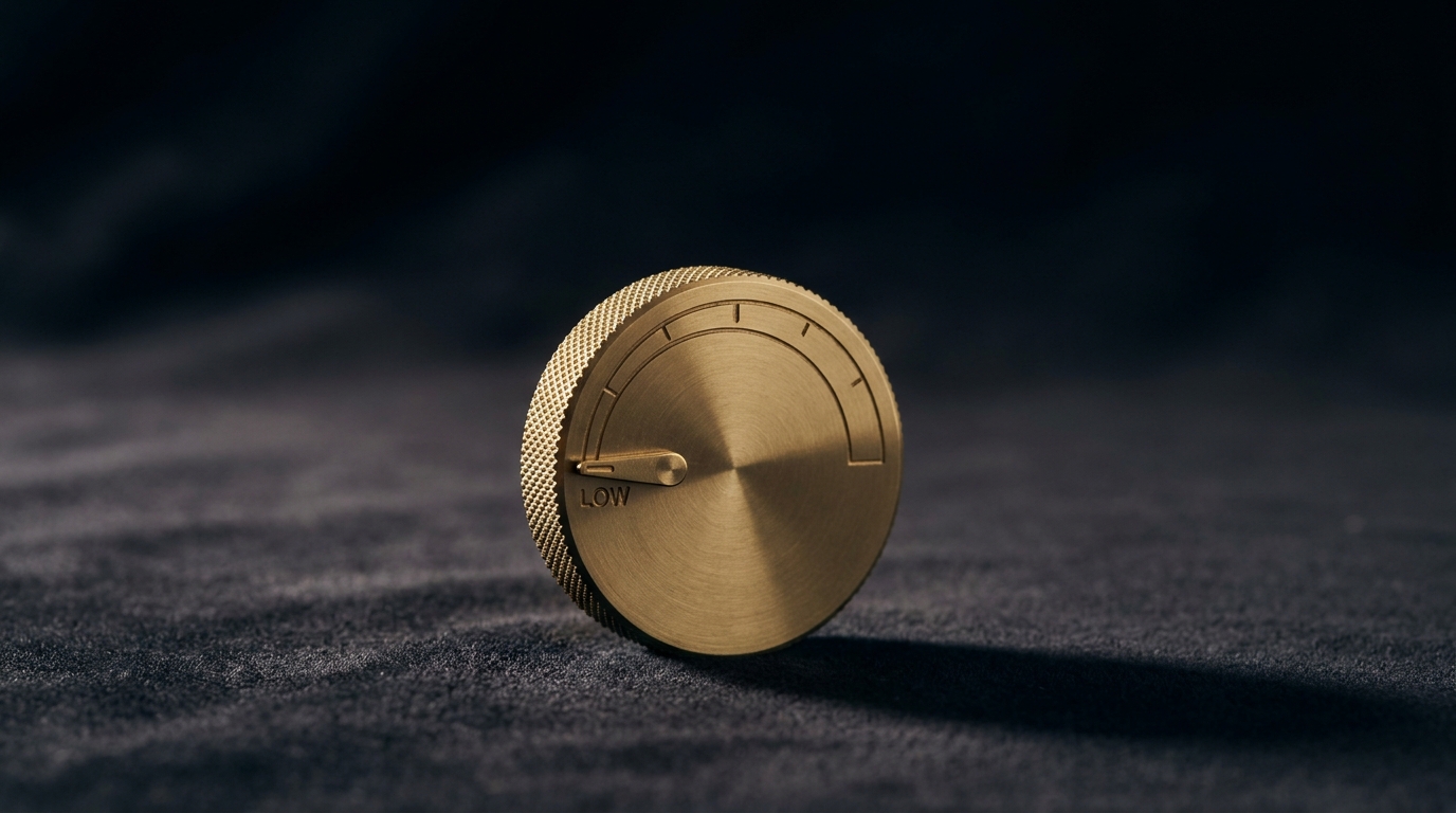 A polished brass control dial turned to a low setting, standing alone on dark charcoal velvet under directional light